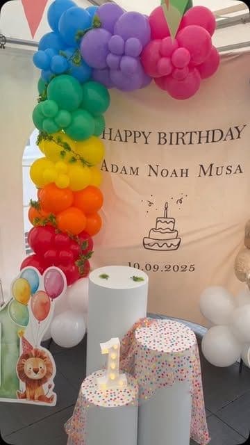 Rainbow balloon arch over a first birthday backdrop