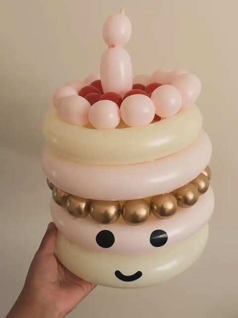 A balloon birthday cake with a candle on top, a band of gold balloons and a smiley face