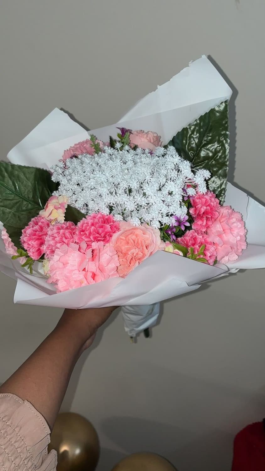 A wrapped bouquet of pink carnations and white gypsophila