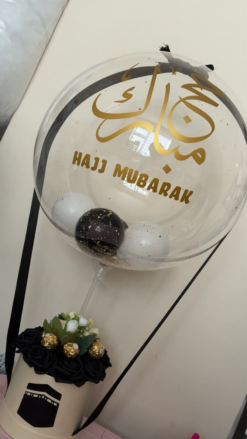 A clear bubble balloon printed with Hajj Mubarak in gold, over a black rose box with Ferrero Rocher