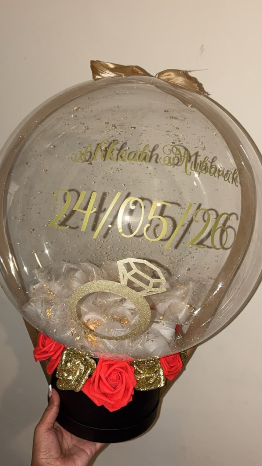 A clear bubble balloon printed with Nikaah Mubarak, a diamond ring and the date 24/05/26 in gold