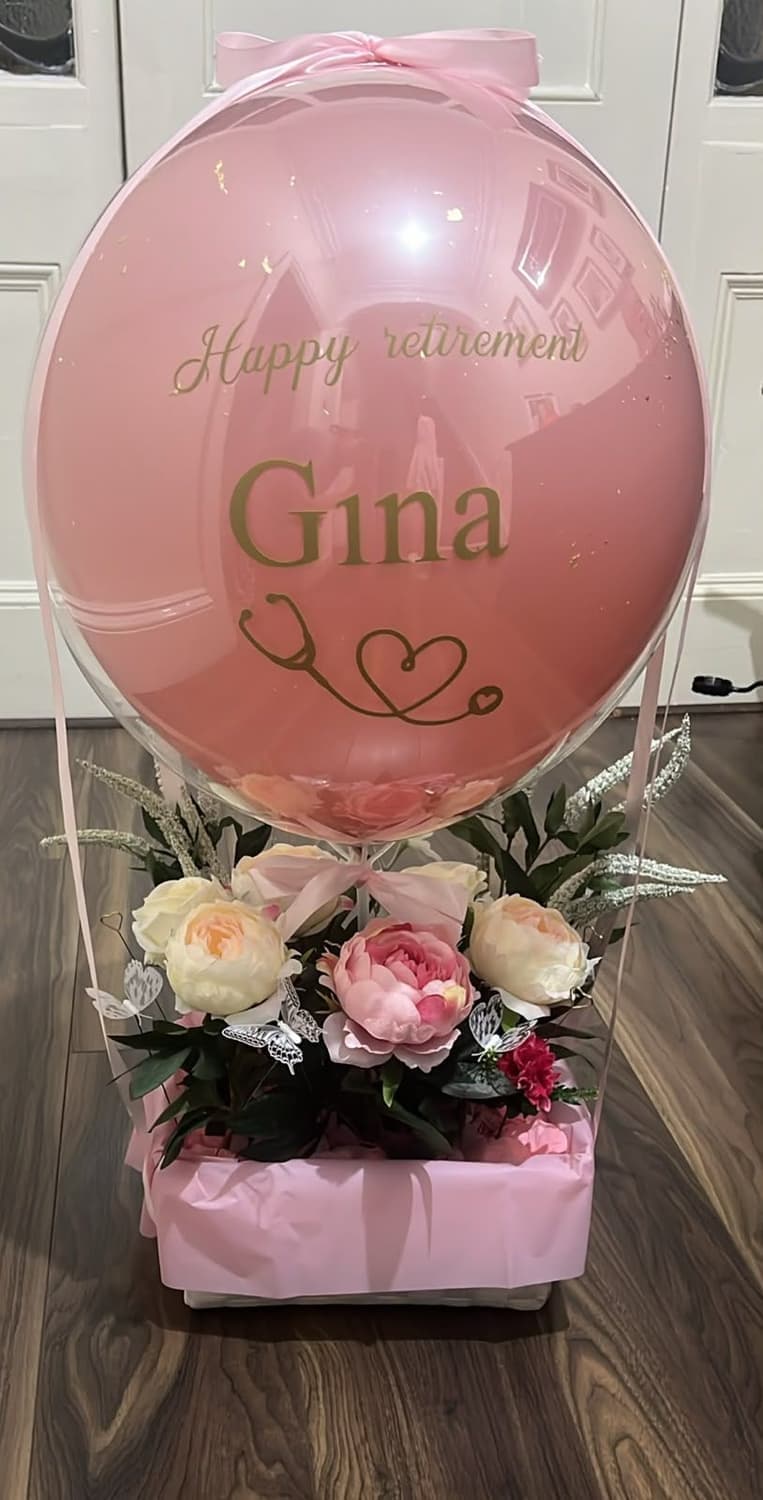 A pink bubble balloon reading Happy retirement Gina above a box of peonies and roses