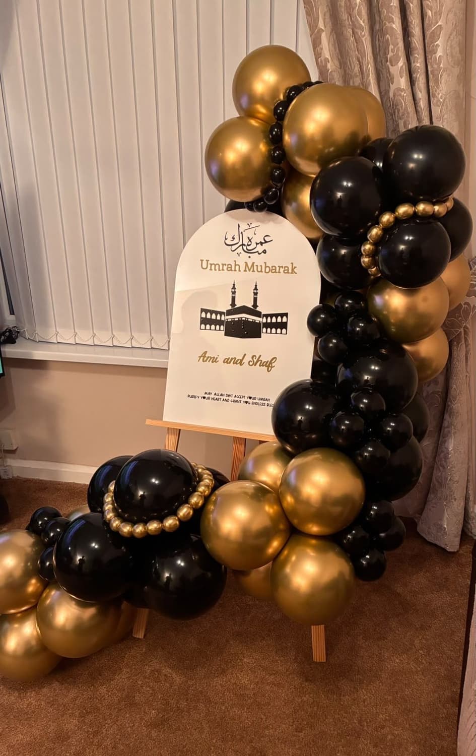A black and gold balloon garland with pearl details beside an Umrah Mubarak sign on an easel